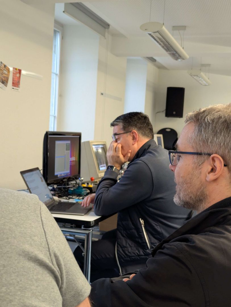 Du siehst Daniel und Allen konzentriert bei der Arbeit, während Giacomo im Hintergrund nachdenklich