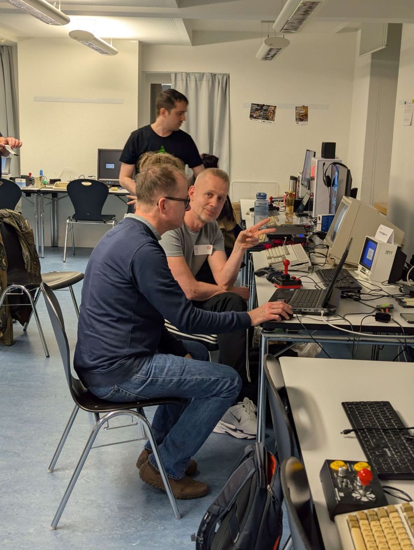 Alen zeigt siegessicher das Victory-Zeichen, während ein Zuschauer an einem seiner Systeme arbeitet.